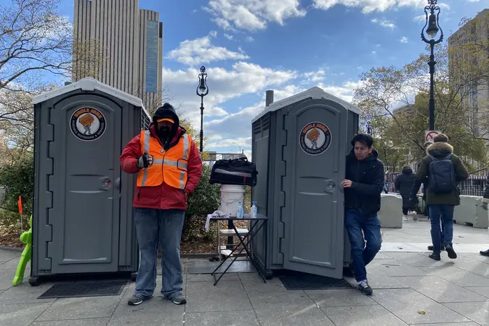 A worker in an orange vest stands in between two port-a-potties at the Manhattan entrance to the Brooklyn Bridge.
